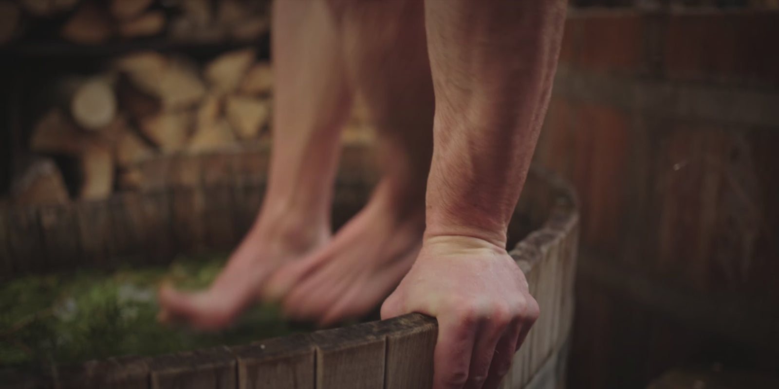 Chill. Fit man in his late 30s jumping into a wooden tub for a cold plunge.